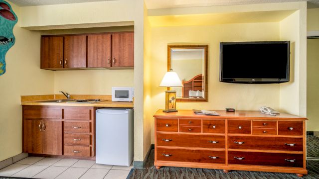 A wide view of a hotel room with a kitchenette, dresser, and TV.