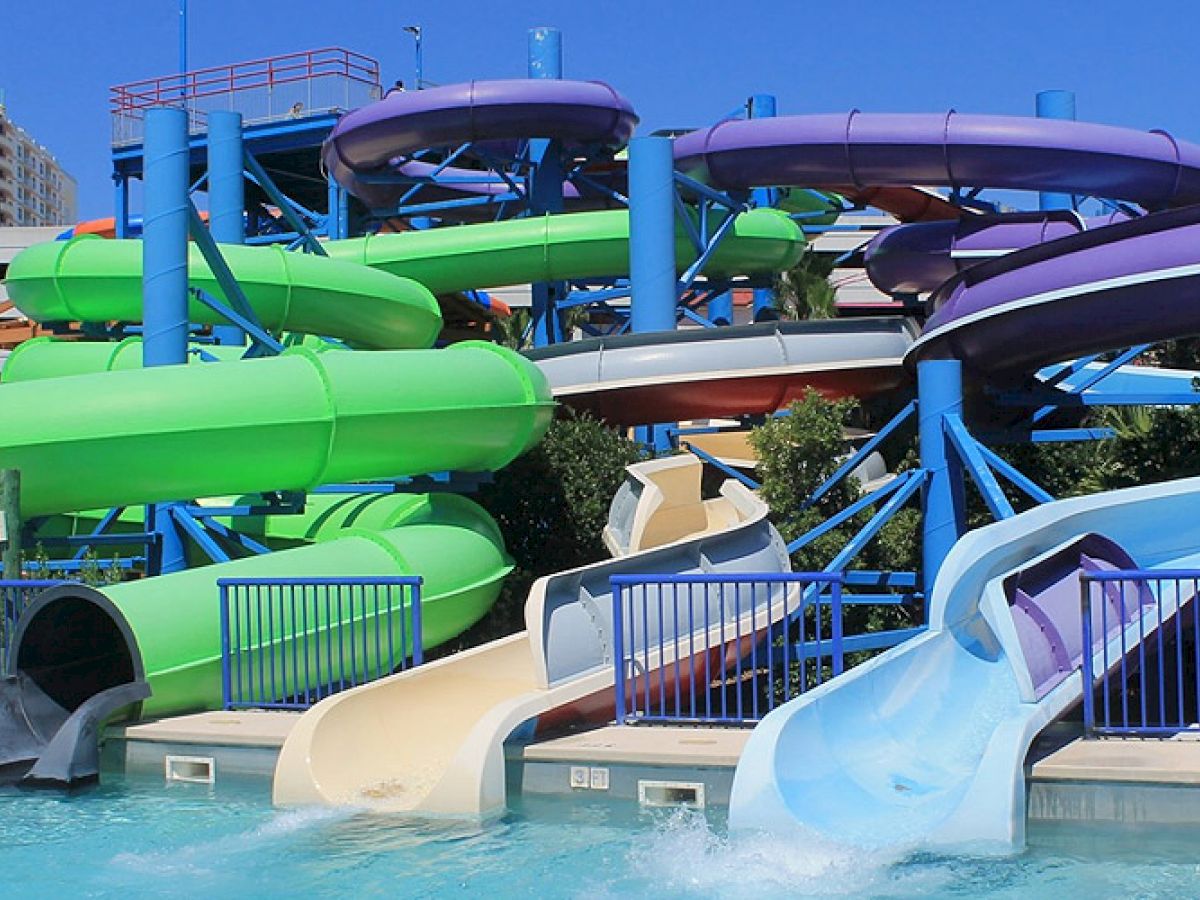 The image shows a water park with multiple colorful water slides, including green, purple, blue, and orange slides leading into a pool.