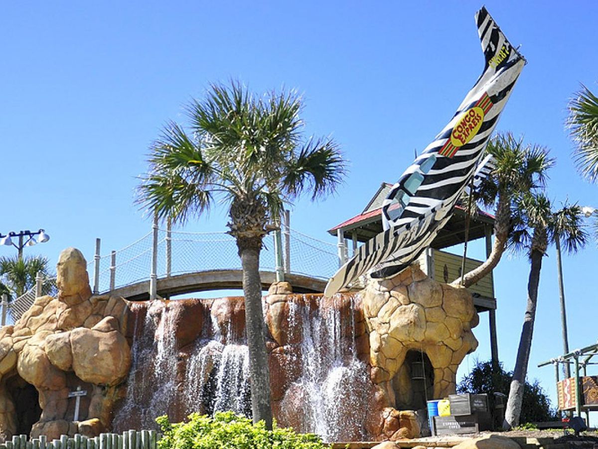 The image shows a tropical-themed mini-golf course with waterfalls, palm trees, and a zebra-striped airplane sticking out of rocky terrain.