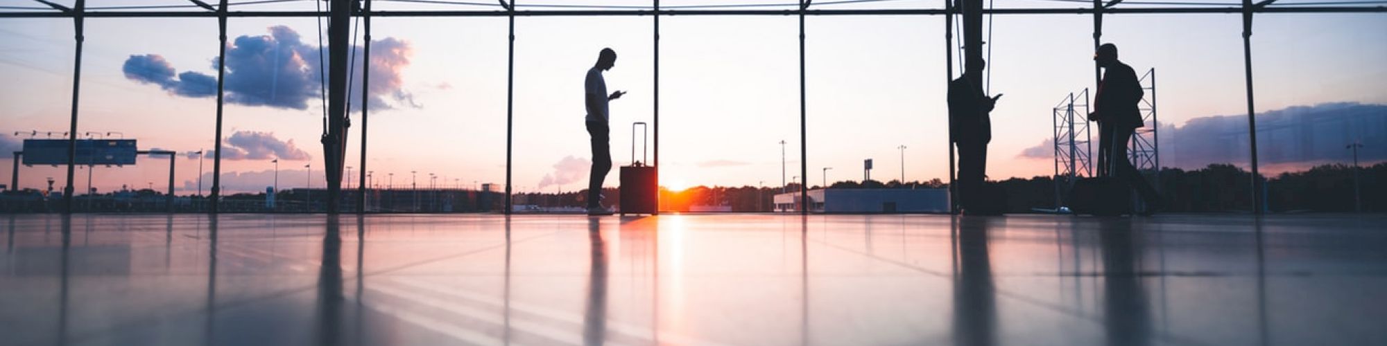 Silhouettes of two people in an airport terminal at sunset, with large windows and a reflective floor. They are standing apart, possibly waiting.