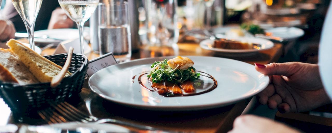A plate of food with a piece of bread and a glass of wine on a restaurant table.