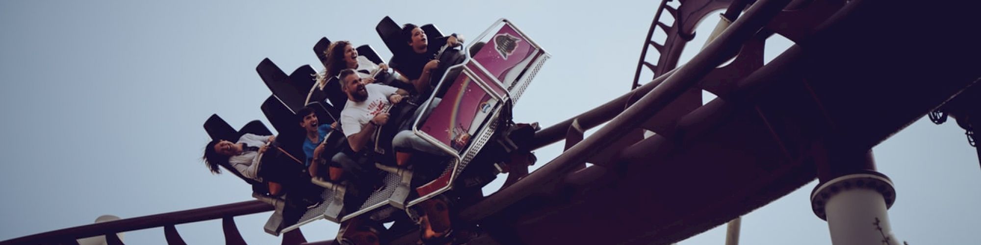 The image shows people riding a roller coaster on a curved track against a cloudy sky, appearing to enjoy the thrill of the ride, ending the sentence.