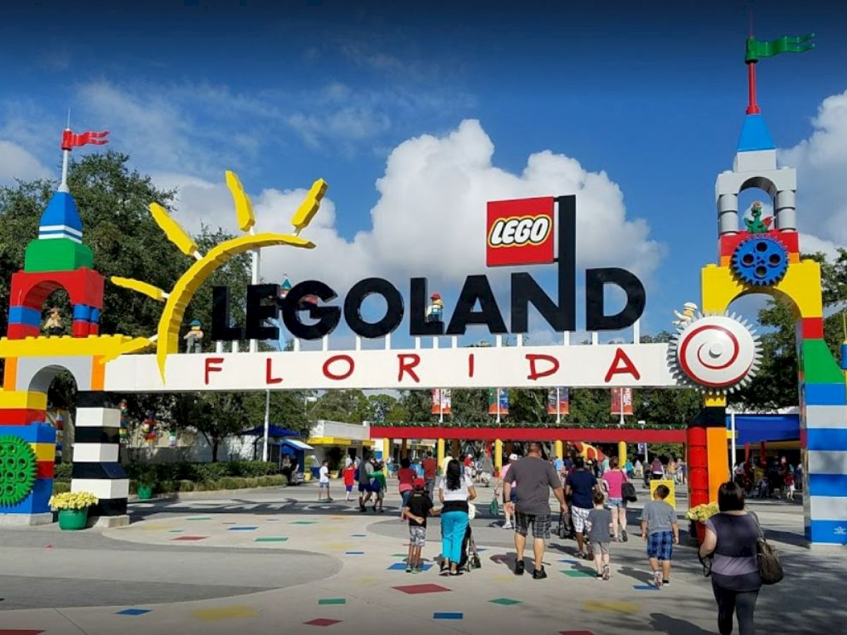 The image shows the entrance of LEGOLAND Florida with colorful LEGO structures and people walking through.