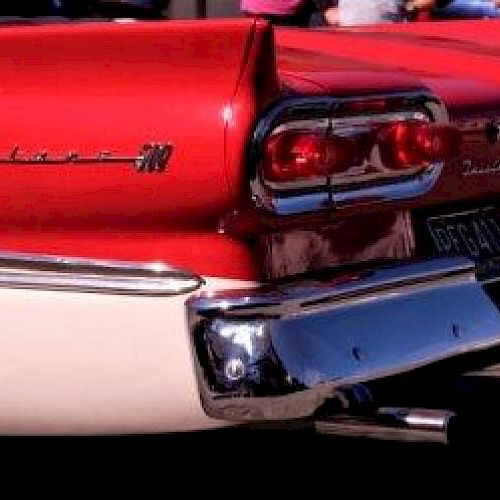 The image shows the rear end of a red and white vintage car with distinctive tailfins and classic taillights, likely from the 1950s or 1960s.