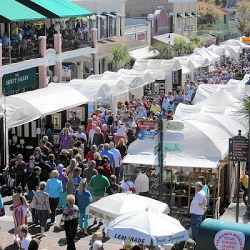 A lively outdoor market with numerous white tents, various vendors, and a large crowd of people walking through the narrow street.