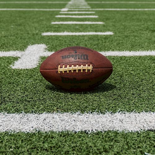 A football rests on a green field with white lines marking the yardage.