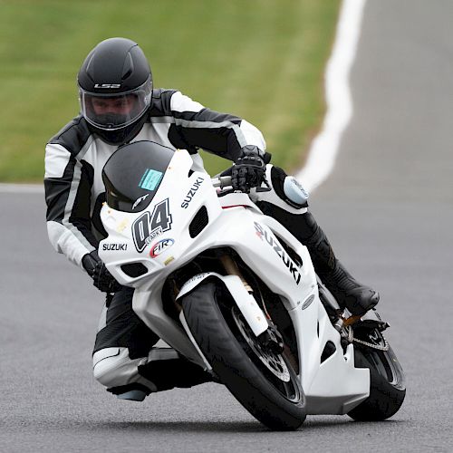A motorcyclist in black and white gear leans into a curve on a white Suzuki bike on a racetrack.