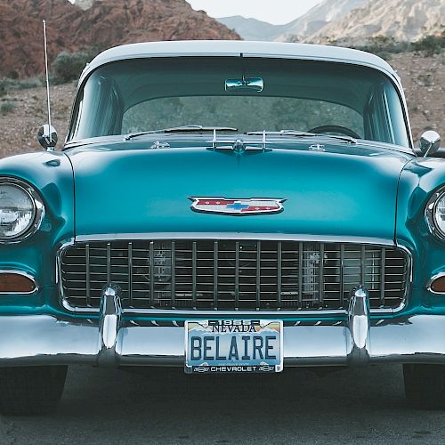 The image shows the front view of a vintage teal Chevrolet Bel Air with a license plate reading "BELAIRE," parked in a scenic outdoor location.