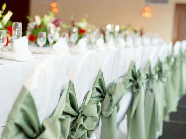A long table set with white tablecloth, green bow-tied chairs, flowers, glasses, and napkins.