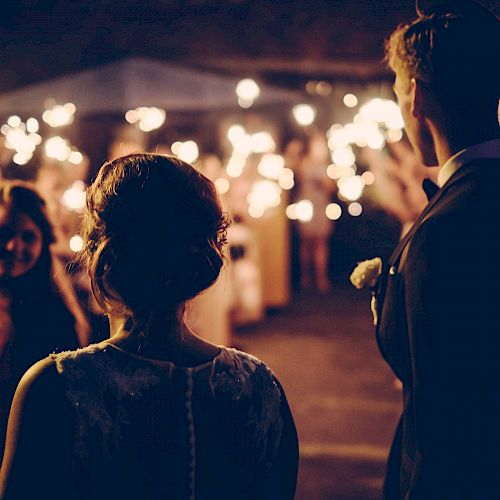 A couple is standing at an event with people holding sparklers in the background, creating a festive and celebratory atmosphere.