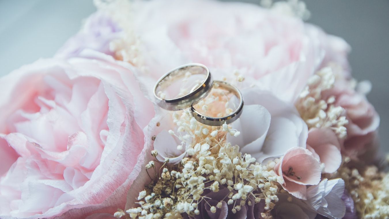 Two wedding rings rest atop a bouquet of pink and white flowers, creating a romantic and elegant scene.