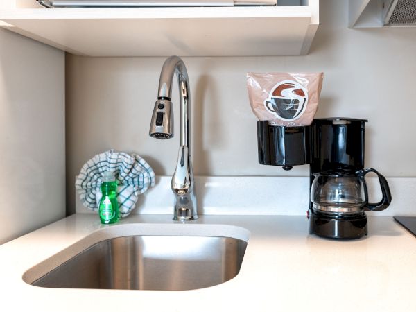 A kitchen sink with a faucet, a coffee maker with a cup holder, a cleaning cloth, and a dish soap bottle on the counter.