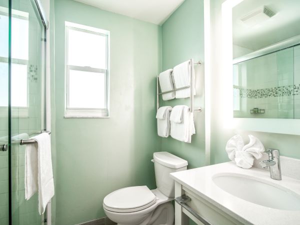 A small, modern bathroom with light green walls, a shower, a toilet, a sink with a mirror, and neatly arranged towels.