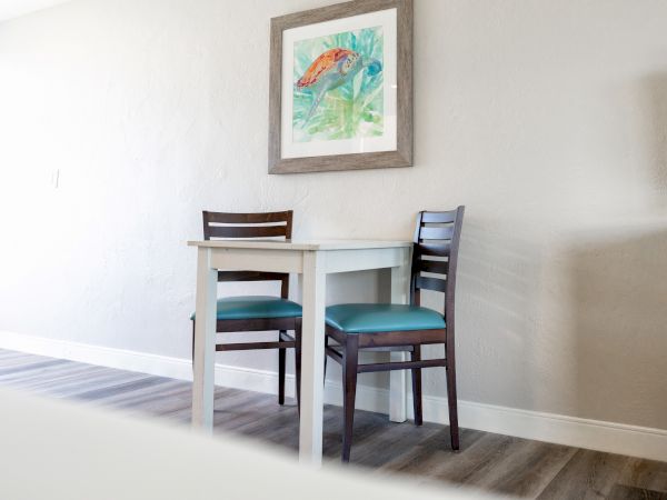 Two chairs with blue cushions are placed next to a small table. A framed artwork hangs above them on the wall.