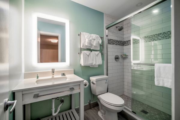 A modern bathroom featuring a backlit mirror, sink, towel rack, toilet, and a glass-enclosed shower with white tiles and a decorative inlay.