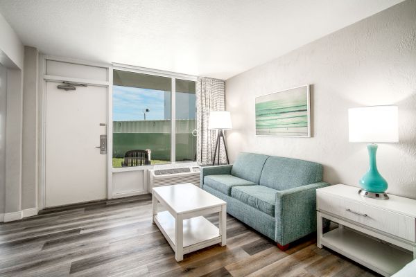 The image shows a modern, well-lit living room with a teal sofa, white furniture, and a large window providing plenty of natural light ending the sentence.