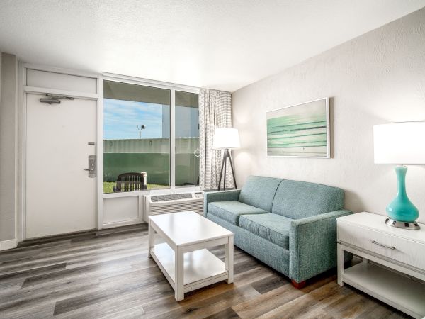The image shows a modern, well-lit living room with a teal sofa, white furniture, and a large window providing plenty of natural light ending the sentence.