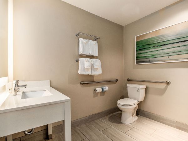 This image shows a clean, minimalistic bathroom with a sink, toilet, towel rack, and a green-themed artwork on the wall, complete.