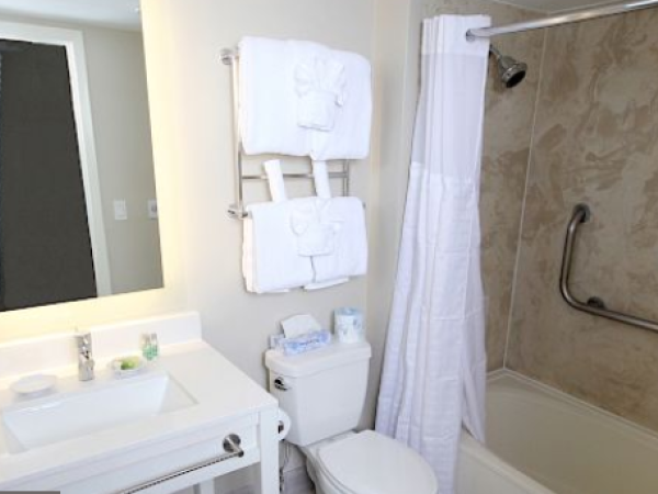 A bathroom with a sink, mirror, toilet, towels on a rack, and a bathtub with a shower curtain and grab bar.