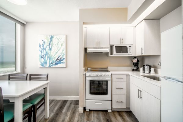 A modern kitchen and dining area with white cabinets, a stove, and a microwave. There’s a dining table with chairs, and a painting on the wall.