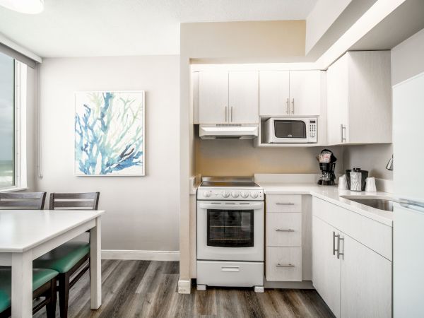 A modern kitchen and dining area with white cabinets, a stove, and a microwave. There’s a dining table with chairs, and a painting on the wall.