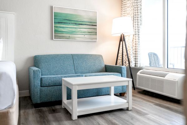 A modern living space with a blue sofa, white coffee table, standing lamp, abstract wall art, and large windows with curtains.