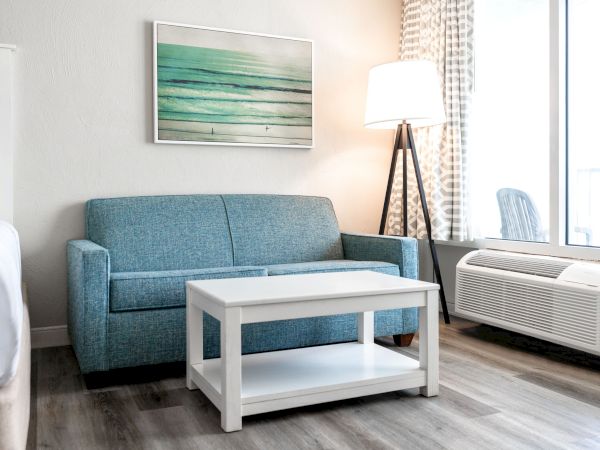 A modern living space with a blue sofa, white coffee table, standing lamp, abstract wall art, and large windows with curtains.