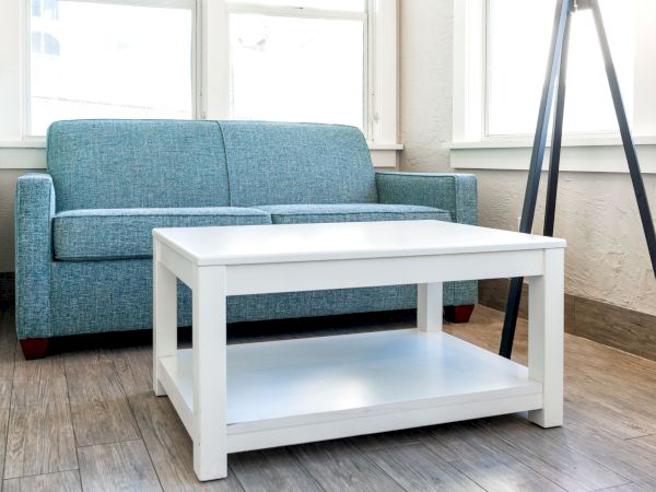 A modern living room features a blue sofa, a white coffee table, and a black tripod stand, with large windows letting in ample light.