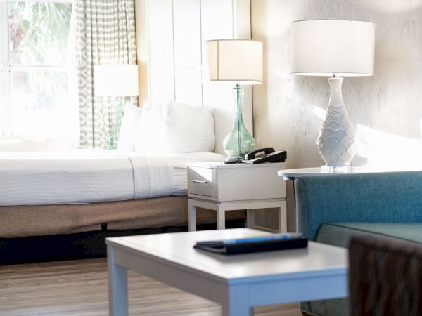 A well-lit hotel room with a bed, nightstands, lamps, a couch, and a coffee table with a closed tablet on it.