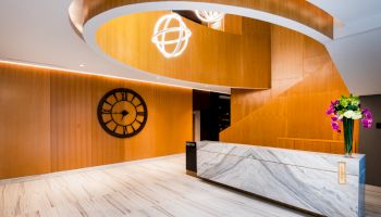 Modern reception area with curved wooden architecture, a large wall clock, marble counter, and floral arrangement.