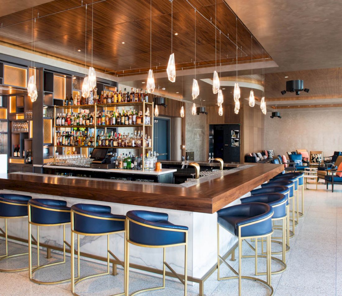 A modern bar with a wooden top, blue stools, and gold accents.