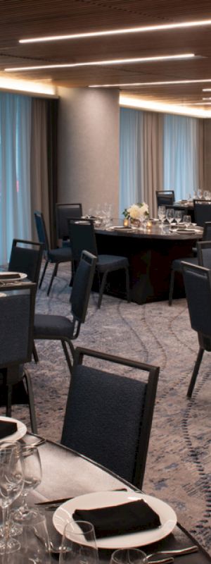 The image shows an elegantly set banquet hall with round tables adorned with black napkins, wine glasses, and flower centerpieces.