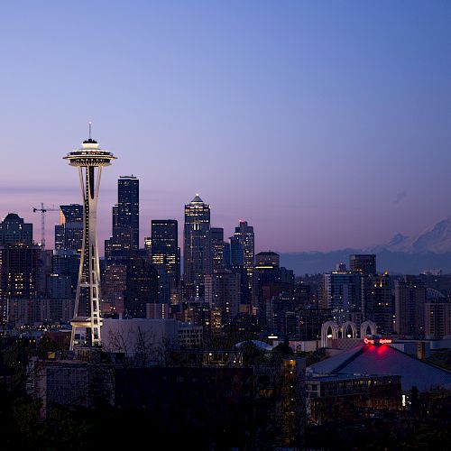 This image showcases the Seattle skyline at dusk, featuring the iconic Space Needle and distant Mount Rainier against a serene, purple-hued sky.