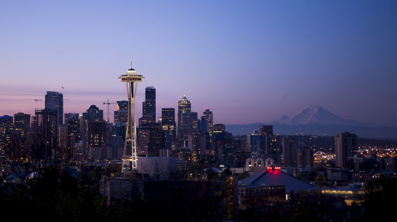 This image shows the Seattle skyline at dusk, featuring the Space Needle and surrounding skyscrapers with Mount Rainier visible in the background.
