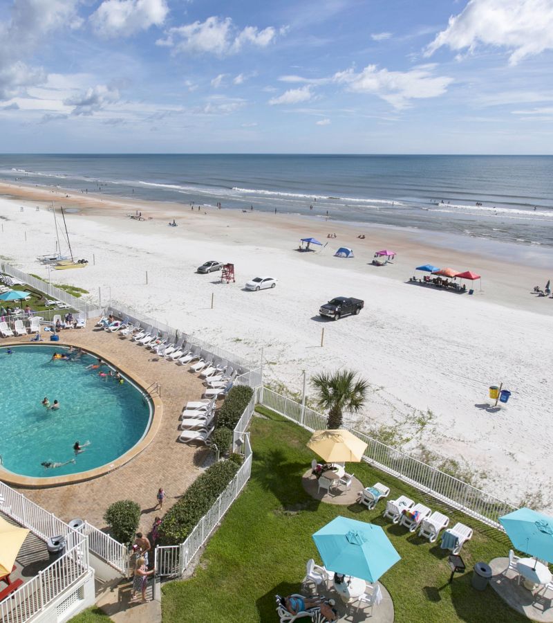 Aerial view of a beachfront pool and lounge area with people swimming and relaxing